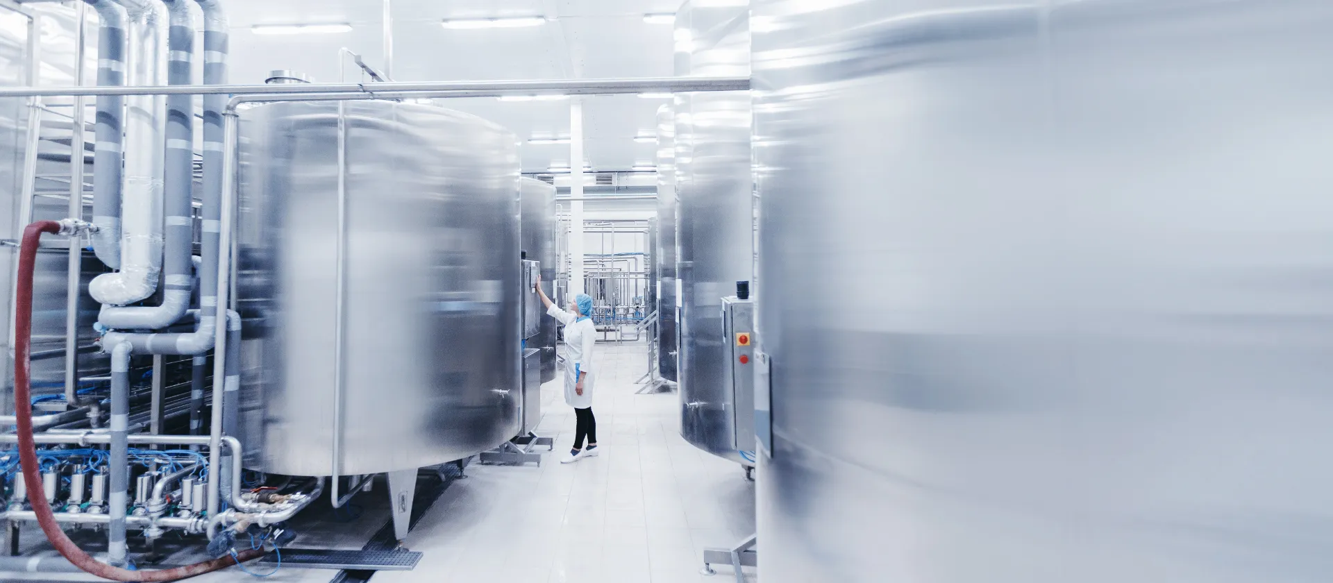 Worker female engineer operator in uniform uses process control panel food factory production line and steel tanker