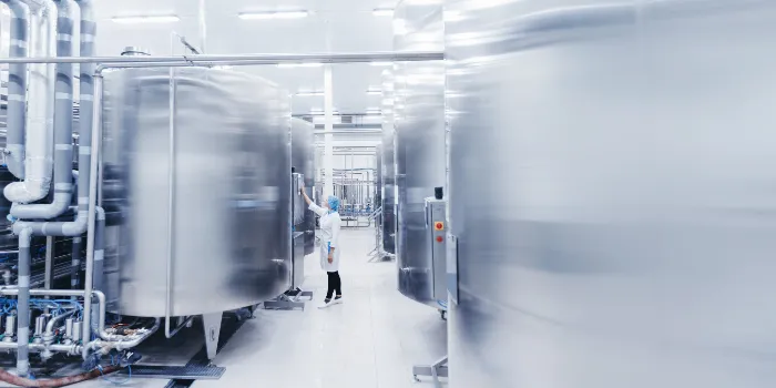 Worker female engineer operator in uniform uses process control panel food factory production line and steel tanker